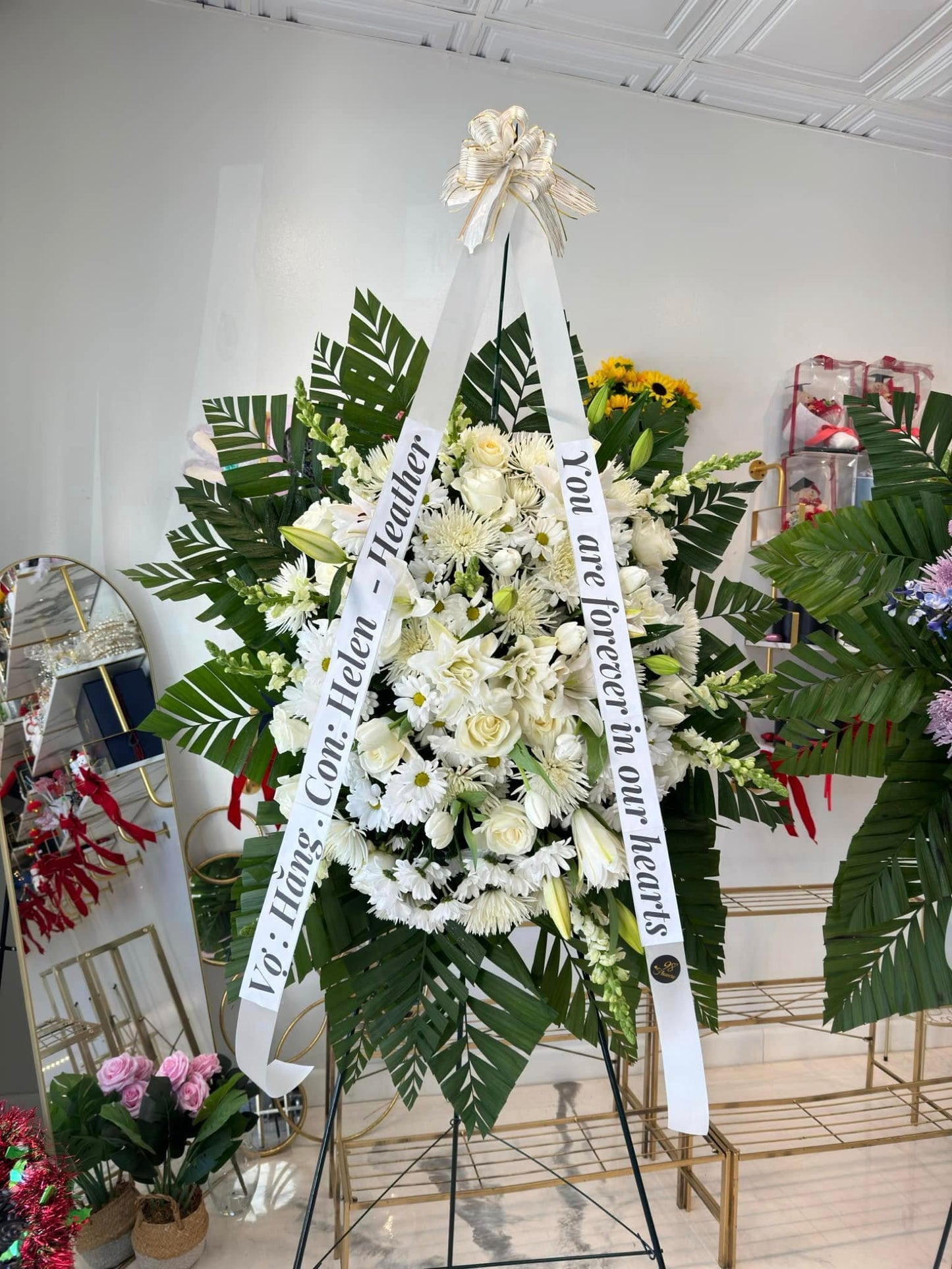 All-white sympathy standing spray with lilies, roses and ribbon