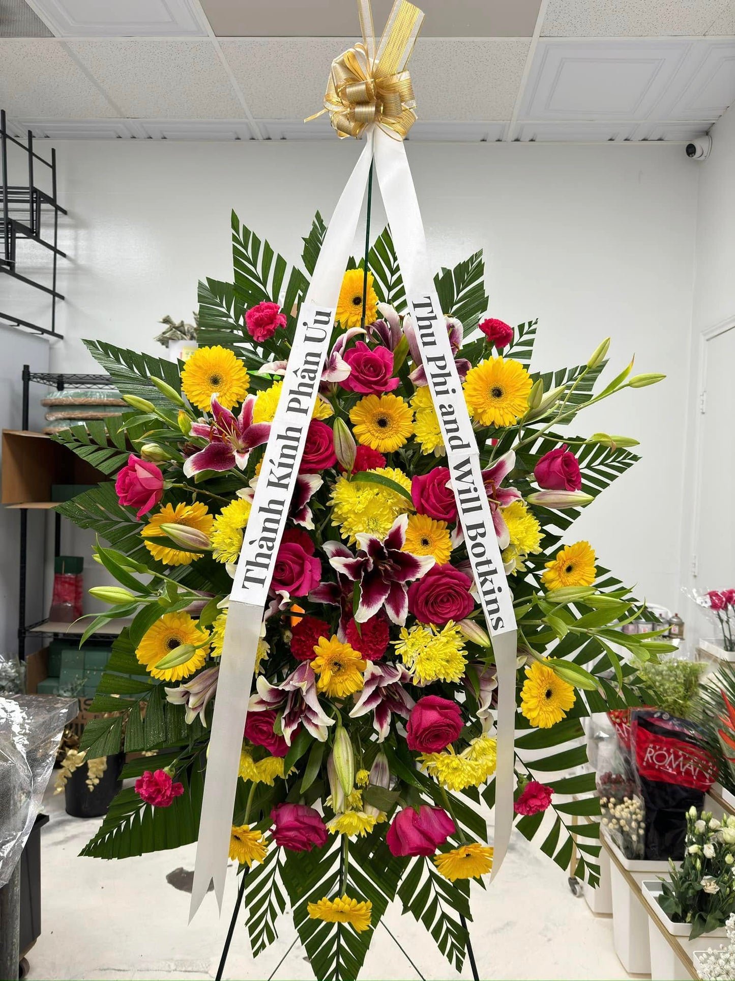 Yellow and red celebration of life standing spray with gerberas, roses and lilies