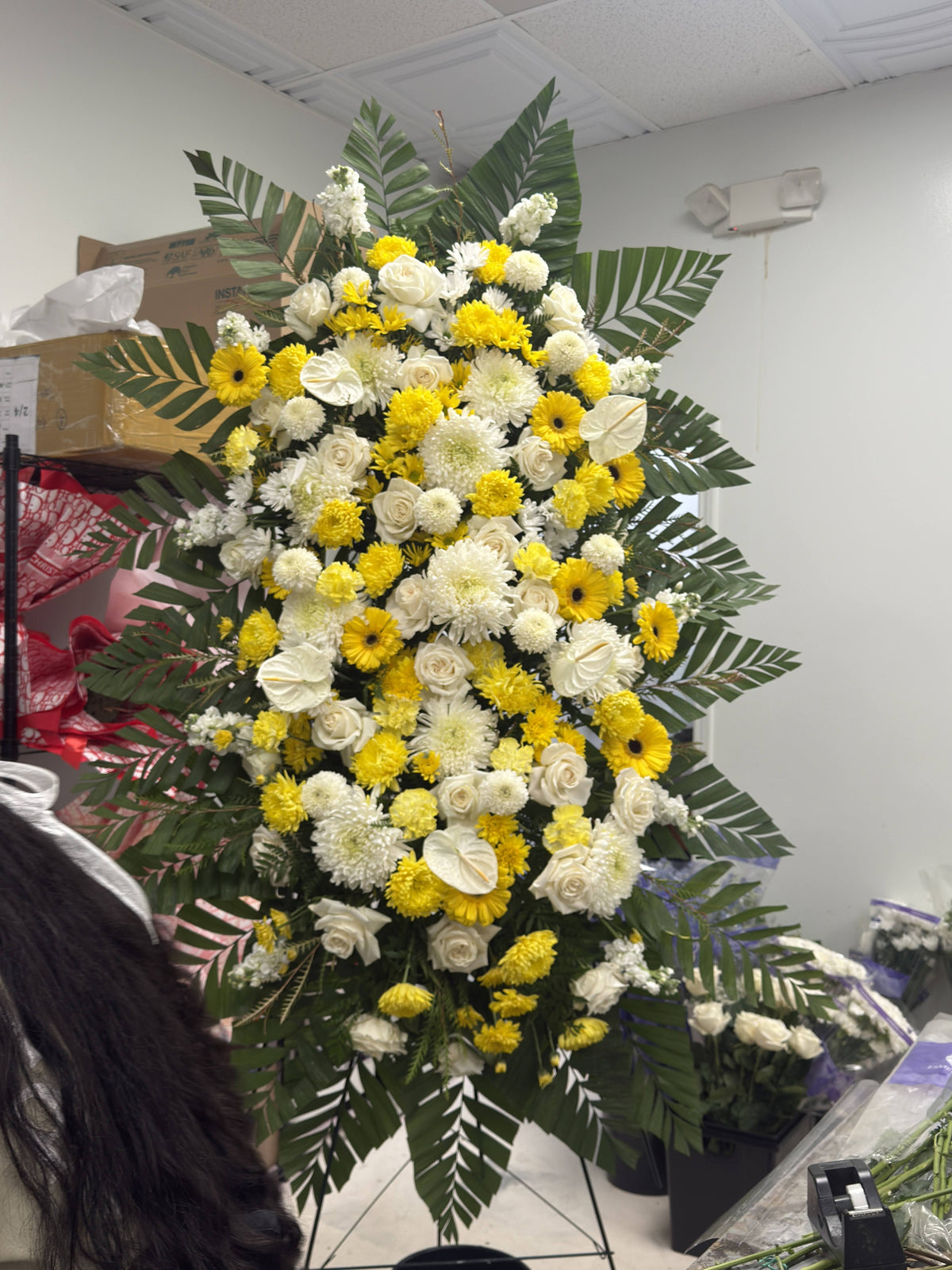 Upright oval sympathy arrangement of yellow and ivory-white flowers framed by green foliage