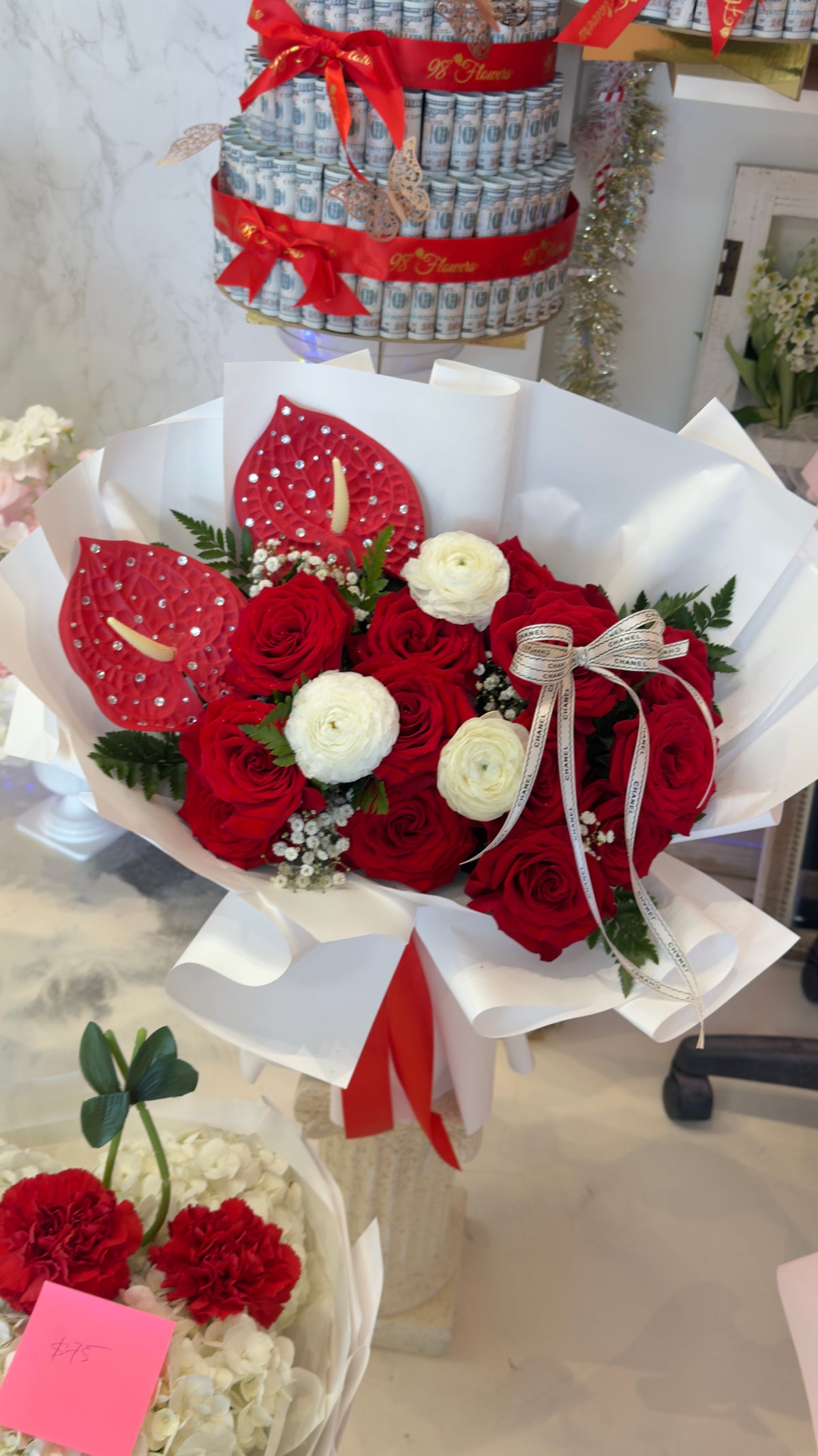 Red rose bouquet with ivory accent blooms, broad red anthurium accents, white wrapping and a red ribbon
