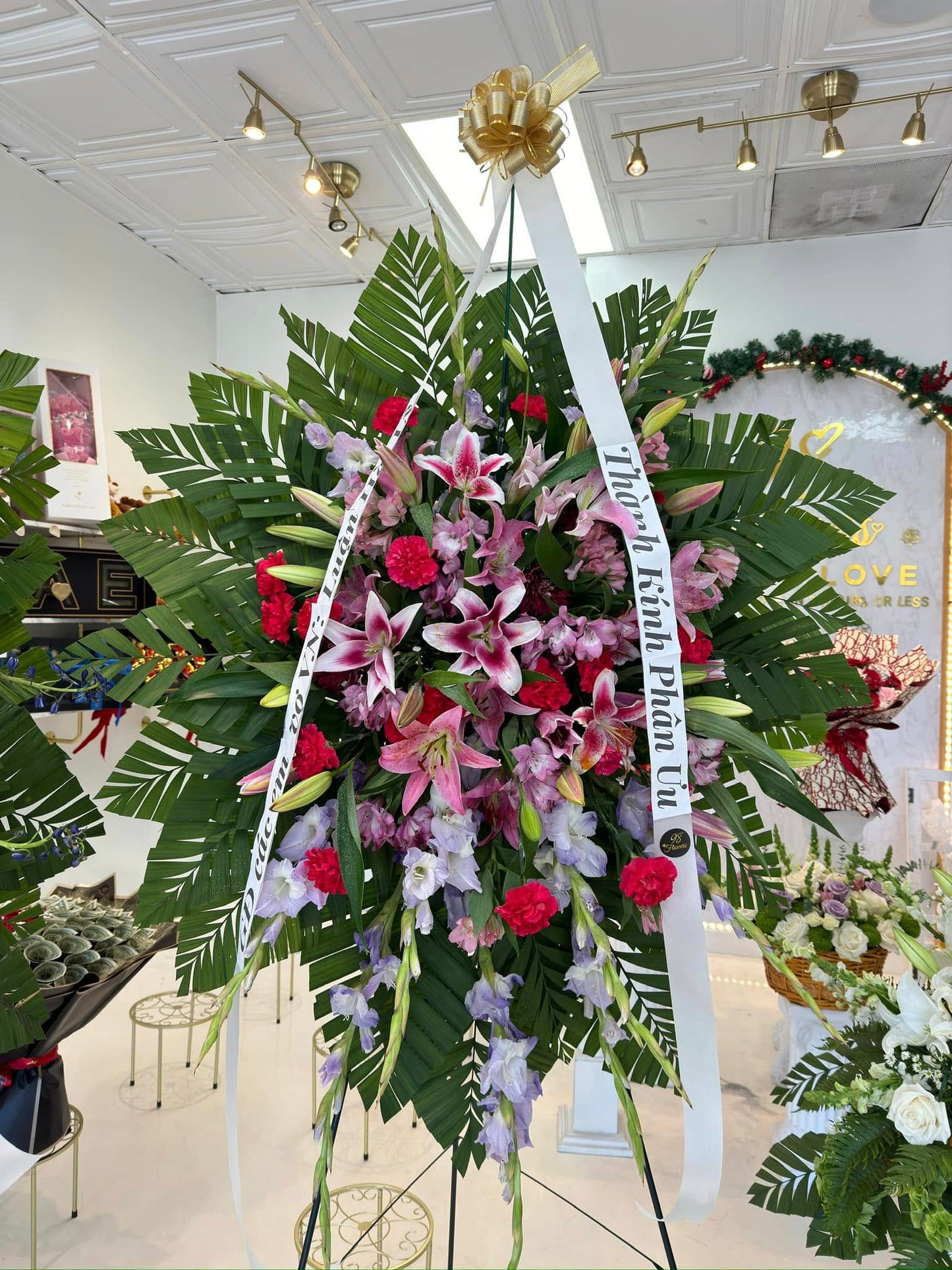 Pink and red lily sympathy standing spray with roses and tropical greenery