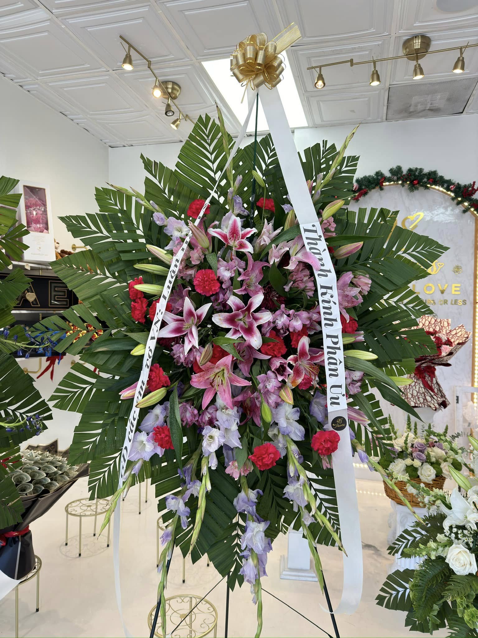 Pink and red lily sympathy standing spray with roses and tropical greenery