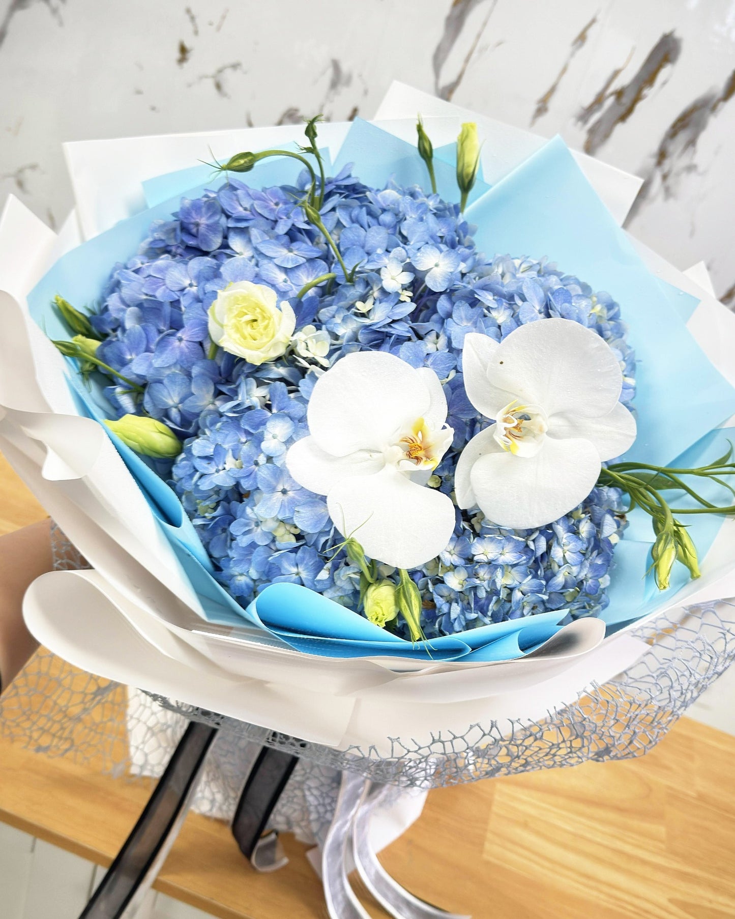 Blue Hydrangea Cloud bouquet with white orchids, cream lisianthus, and silver mesh