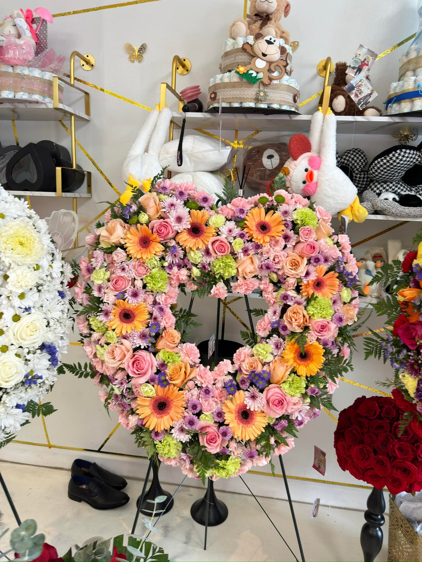 Pastel heart sympathy wreath with pink roses, orange gerbera daisies and purple flowers on a standing easel