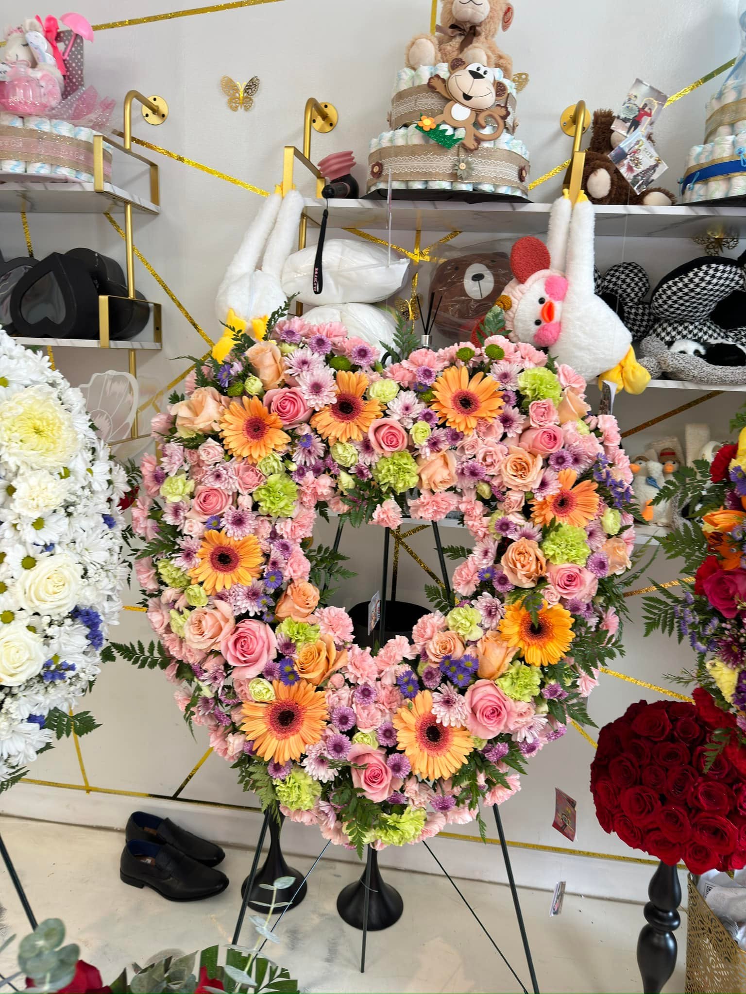 Pastel heart sympathy wreath with pink roses, orange gerbera daisies and purple flowers on a standing easel
