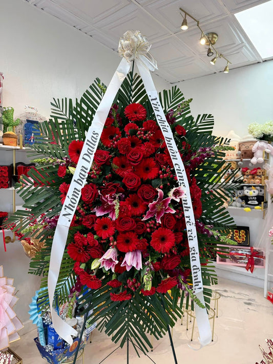 All-red sympathy standing spray with roses, gerberas, lilies and tropical greenery