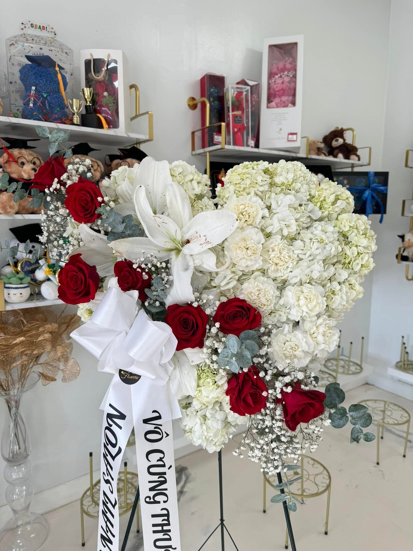 White heart sympathy wreath with red roses, lilies and condolence ribbon
