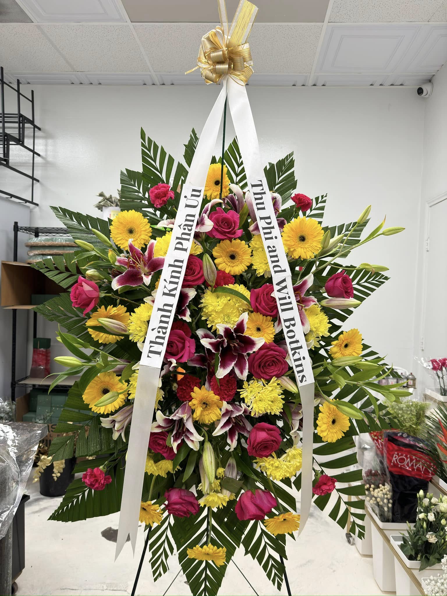 Yellow and red celebration of life standing spray with gerberas, roses and lilies