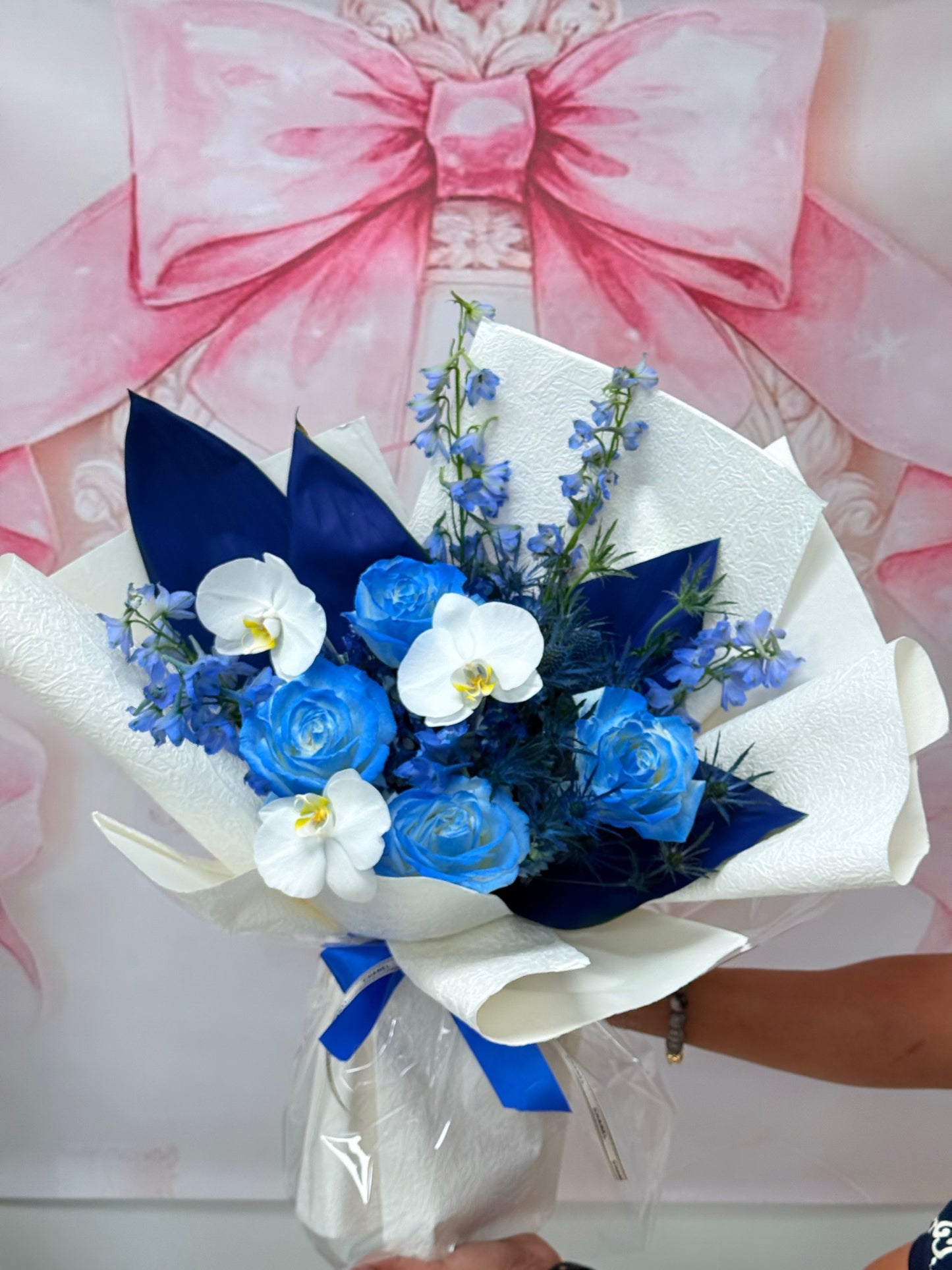Blue roses and white orchids in a white and navy wrapped bouquet