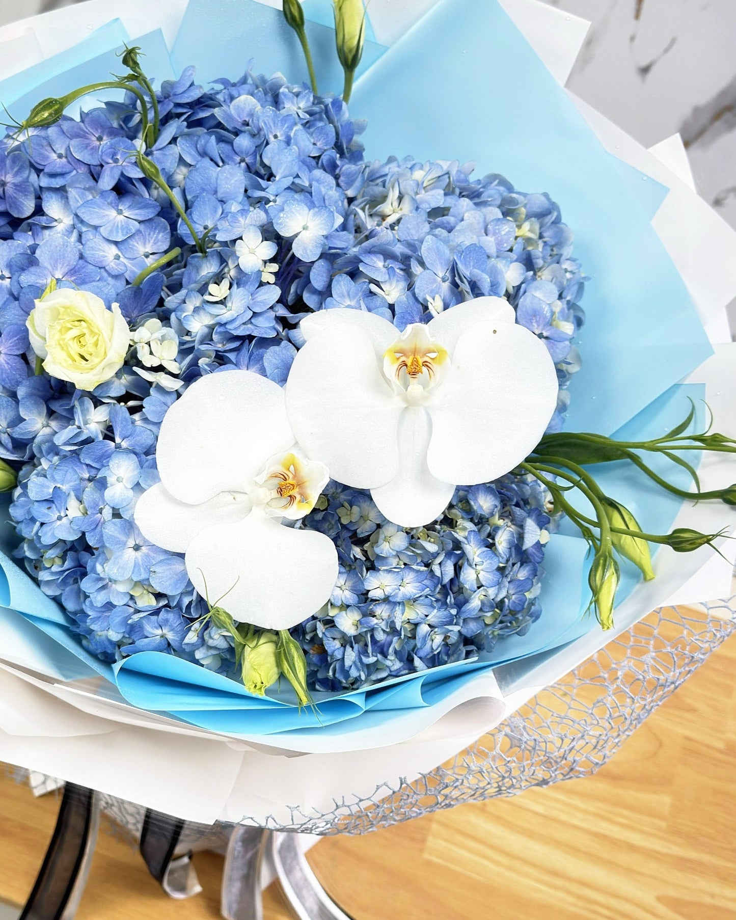 Close-up of blue hydrangeas, white phalaenopsis orchids, and cream lisianthus