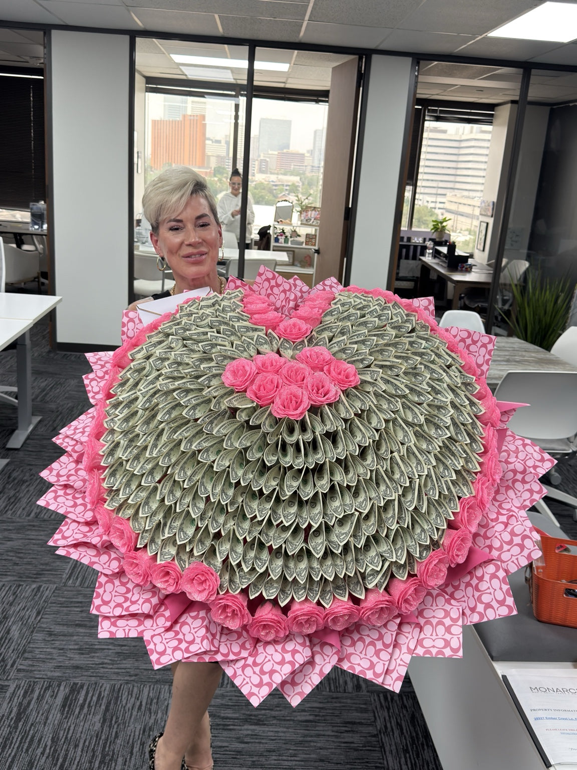 Woman holding a giant heart-shaped money bouquet with pink roses and 200 one-dollar bills