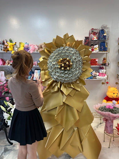 Person standing beside oversized golden $100 money flower arrangement