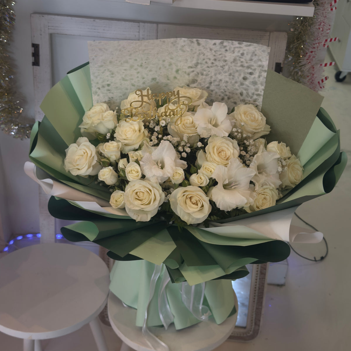 Cream roses and white flowers in layered sage-green wrapping tied with a pale green ribbon