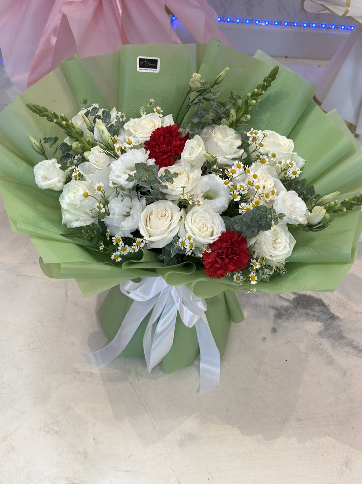 Round white rose bouquet with deep red accents, smaller white flowers, greenery, sage-green wrapping and a white bow