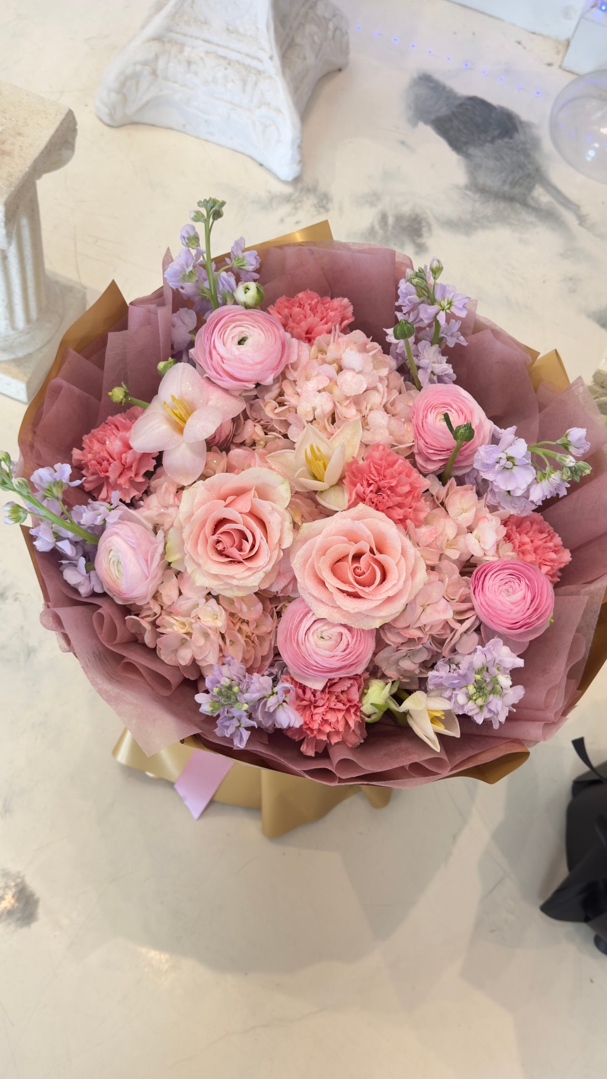 Mixed bouquet of pink and cream roses with pale blooms and purple accents in mauve and brown wrapping