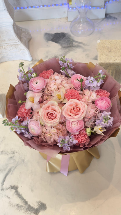 Mixed bouquet of pink and cream roses with pale blooms and purple accents in mauve and brown wrapping, alternate view 1