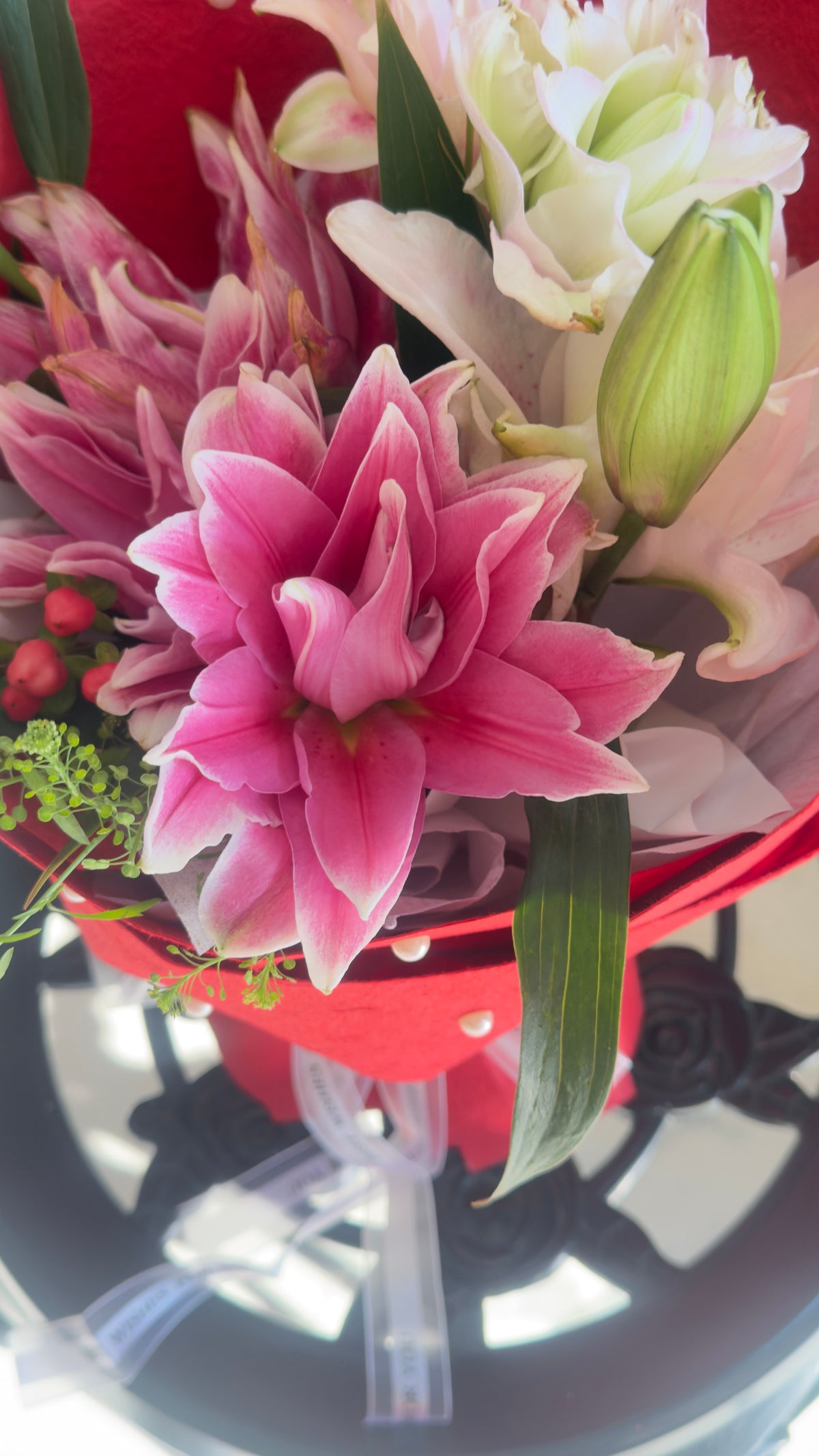 Pink and white lily bouquet with green buds in red wrapping dotted with small pearl-like white details, alternate view 1